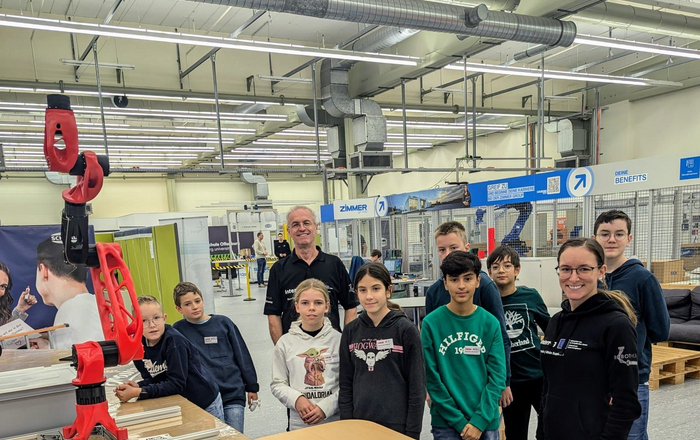 Ein Mann und eine Frau mit einer Gruppe von Kindern stehen neben einem Tisch mit einem Roboterarm